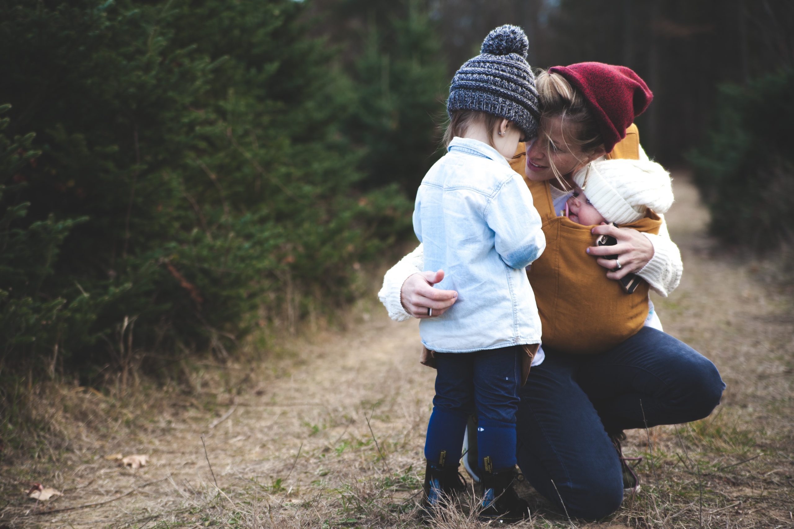 woman outdoors holding baby and hugging toddler