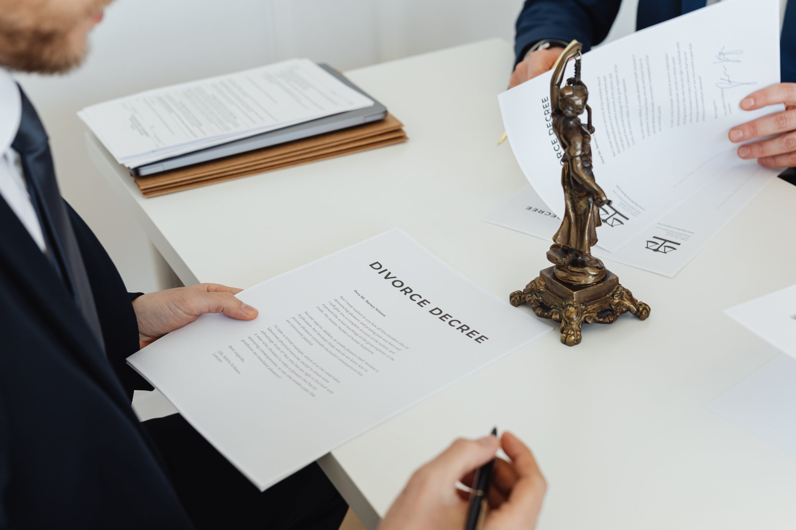 person in a suit holding a divorce decree and pen over a table with other papers on it